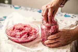 Old granny putting sour cabbage from jar into glass bowl photo