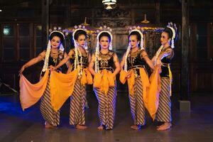 a group of Javanese dancers holding yellow shawls while dancing on stage photo