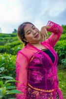 an Asian woman in a traditional pink costume is standing very elegantly in a tea plantation photo