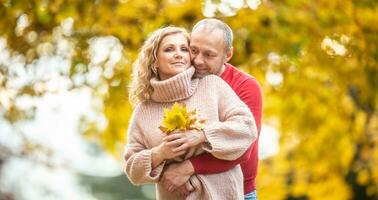 Couple shares their love hugging, holding fallen autumn leaves surrounded by yellow trees photo