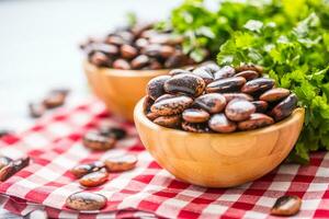 Uncooked beans in wooden bowles  with parsley herbs on kitchen table photo