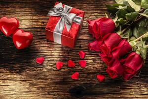 Valentine wedding concept. Bouquet of roses and wrapped gift with red hearts on wooden table photo