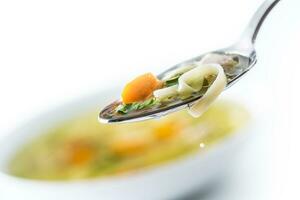 Spoon full of chicken or beef soup with noodles carrot and herbs photo