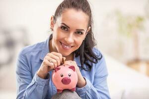 Beautiful female saves money by putting coins into a piggy bank photo