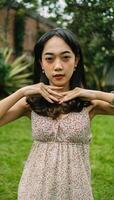 an Asian woman in a patterned dress posing with her hands in a garden photo