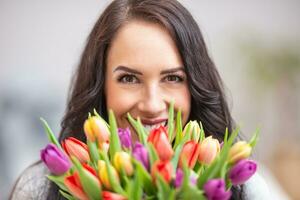 contento oscuro peludo mujer participación un encantador ramo de flores lleno de tulipanes durante nacional De las mujeres día foto