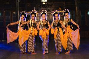 a group of Javanese dancers holding yellow shawls while dancing on stage photo