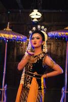 a Javanese dancer in jasmine and a yellow shawl takes selfies on stage after finishing dancing photo