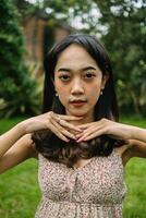 an Asian woman in a patterned dress posing with her hands in a garden photo