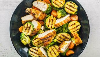 Grilled chicken breast zucchini broccoli and carrot in black plate. Greek or mediterranean food photo