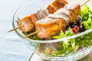 Grilled salmon skewers with summer lettuce salat pomehranate seeds olive oil and dressing. Healthy fish food with fruit and vegetable photo