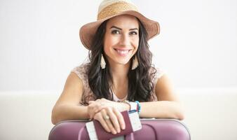 Beautiful woman traveler ready for a flight with her ticker and passport in hands, hat on, smile on face and luggage photo