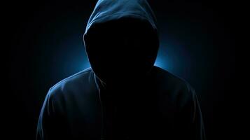 Unrecognizable figure in dark blue hoodie concealed face arms crossed solitary in darkness. silhouette concept photo