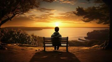 A bench in front of a sunset view with a boy sitting on it. silhouette concept photo