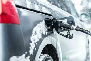 combustible pistola izquierda dentro el coche durante gasolina o gasolina recargar a el estación en congelación invierno hora foto