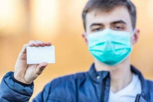 Young man with protective mask on his face holding emty white card.. Protection against virus dust or smog. Coronavirus Covid-19 concept photo