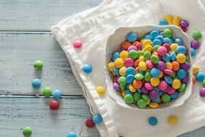 Top view of a bowl full of colorful sweets on a white rug and vintage wood with some scattered around photo