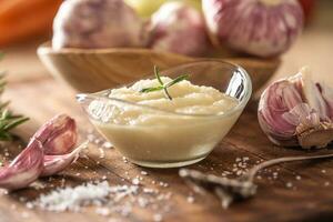 Garlic paste in a glass bowl with peeled garlic, salt and garlic heads photo