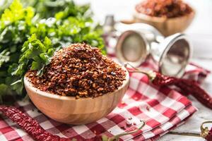 Dried and crushed chili peppers in wooden bowles with parsley herbs photo