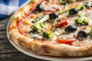 Irtalian pizza with broccoli spinach tomatoes olives and mozzarela or parmesan cheese. Mediterranean vegetarian meal photo