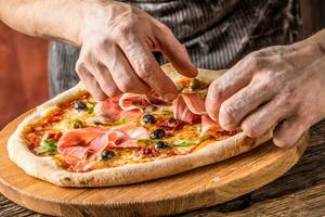 Pizza and Chef. Chef in the restaurant prepares a pizza and decorates it with  prosciutto photo