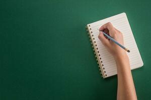 estudiante de el niña mano desde un lápiz con cuaderno en un verde antecedentes foto