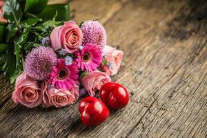 Beautiful bouquet of flowers with two red hearts on wooden table photo