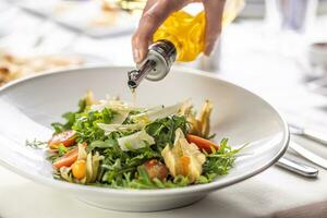 Olive oil pouring over a fresh rocket salad with parmesan shavings and physalis photo