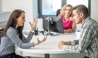 Woman gesticulates to a man angry over disagreement with demale mediator sitting behind the table in the background photo