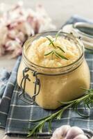 Aromatic garlic paste in a glass jar laid on rustic kitchen cloth with bulbs and peeled cloves and rosemary photo