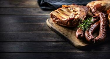 Smoked pork sausages, ribs and neck on wooden board with copy space photo