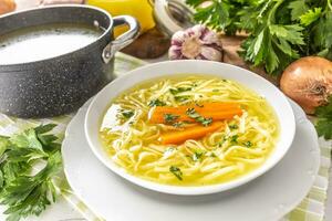 Chicken soup broth in a plate carrot onion celery herbs garlic and fresh vegetables photo