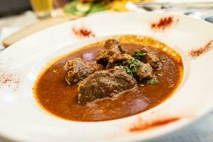 Beef stew with large chunks of meat served in a white plate photo