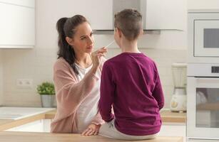Home testing for Covid-19 as mum puts swab into the nose of her son sitting on a kitchen desk photo