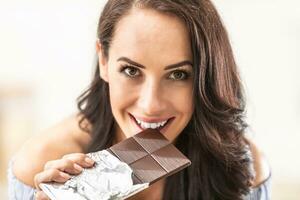 Seductvely looking woman bits off a chocolate bar, smiling photo