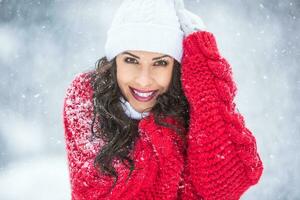 Fashionable woman dressed in warm winter knitted outwear smiles at the camera during snowy winter cold day photo