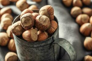 Close up of a vintage metallic mug full of hazelnuts with more nuts on a textile table cloth around it photo