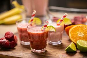 Different colors of red and pink smoothies in cups with paper straws on a kitchen table photo