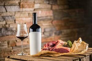 Cup and a bottle of red wine and raw beef steak on wooden table photo