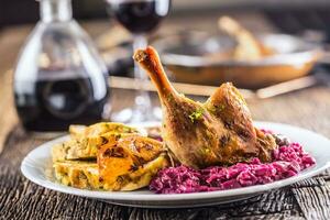 Portion of roast duck leg red cabbage homemade dumplings on plate and red wine on the background photo