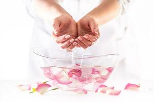 Female hands lifted from water in a glass bowl full of flower petals in a white environment photo