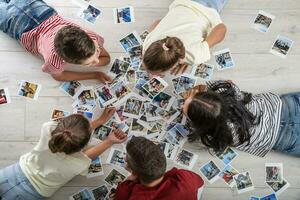 Top view of family with children lying on the floor surrounded by memories on printed photographs surrounding them photo