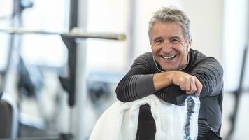 Fit in his sixties, man rests on a towel smiling inside the gym photo