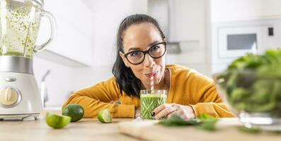 A funny young woman drinks a green smoothie that she made herself. photo