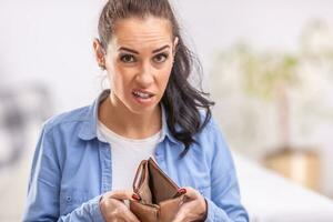 Woman with unsure facial expression holds empty waller or purse open with no money in it photo