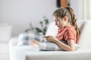 Young preteen girl looks into her phone while having comfortable time at home photo