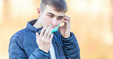 Young man puts protective mask on his face. Protection against virus dust or smog. Coronavirus Covid-19 concept photo