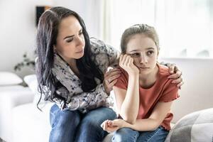 Offended young daughter sulks on a couch while her mother tries to talk to her photo