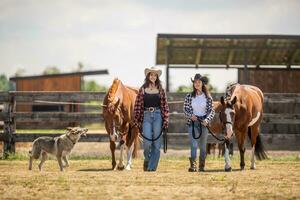 Two young female friends are walking their horses for a ride with their dog running around photo