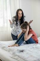 Domestic non-physical violence as woman shouts at a young girl who covers her ears sitting on a bed photo